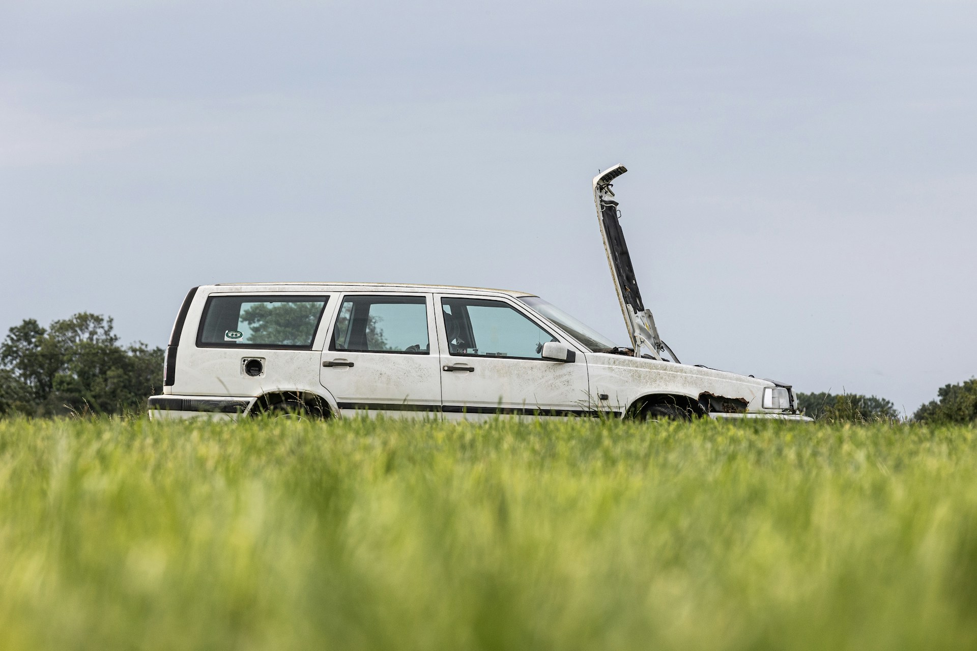 Auto i polityka transportowa miasta Stary biały samochód z otwartą maską stojący w trawie