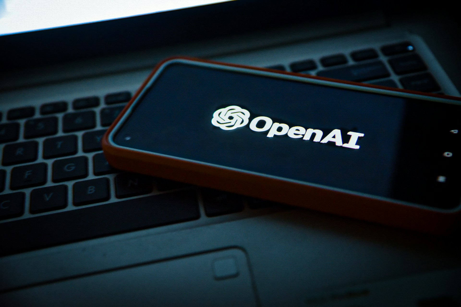 Smartfon z logo OpenAI leży na klawiaturze laptopa.