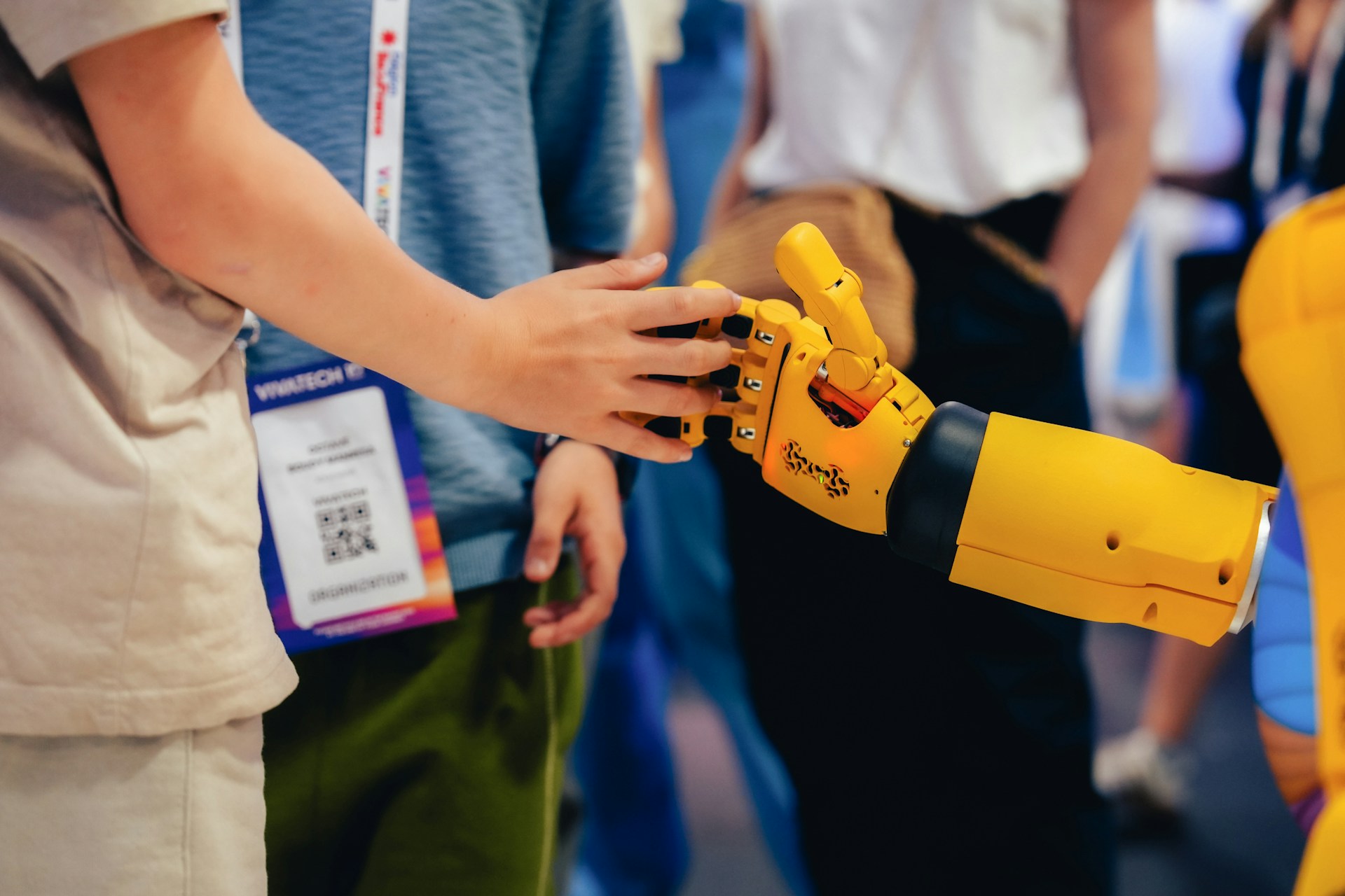 Osoba dotykająca ręki żółtego robota na wydarzeniu technologicznym, reprezentująca kontrolę człowieka nad AI